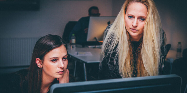 What Is Your Social Media Investigation Solution Missing? - Two women standing behind a computer monitor.