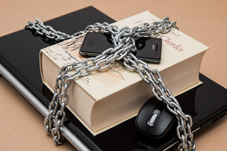 A laptop, computer mouse, book, and smart mobile phone locked in chains